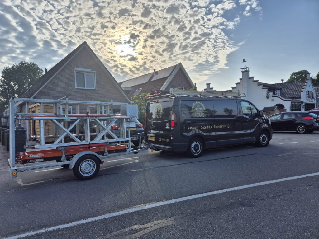 Zwarte bedrijfsbus van Timmer & Onderhoudsbedrijf Keus met aanhanger vol ladders, geparkeerd bij woningen in een woonwijk.
